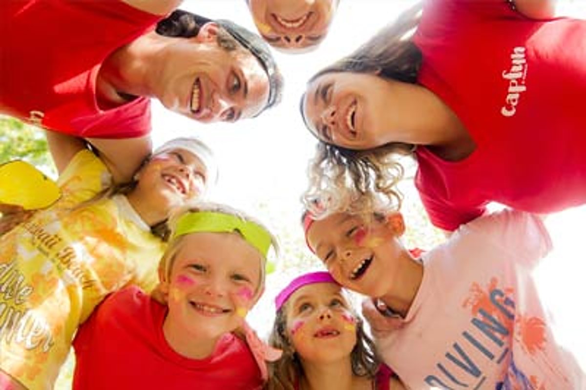 Vue en contre-plongée d’enfants maquillés et d’adultes en t-shirts colorés, penchés les uns vers les autres en souriant.